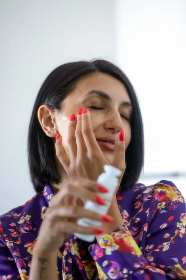 Woman applying cream on her face holding a serum bottle